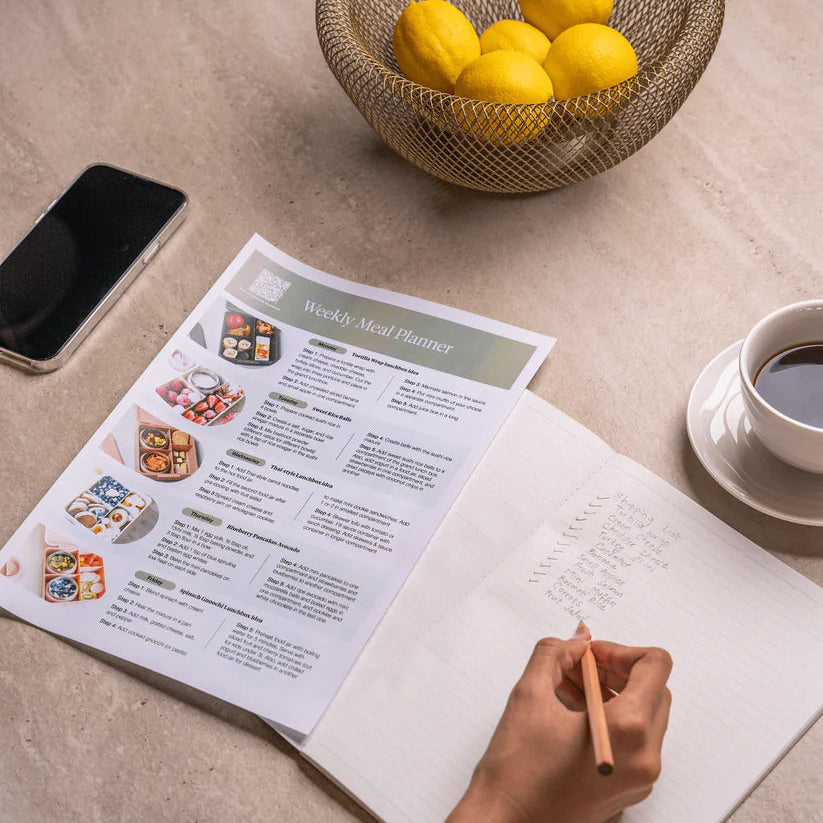 Free_download_weekly_Planner_Person planning a weekly menu with a notebook, pencil, smartphone, and lemons on a table.